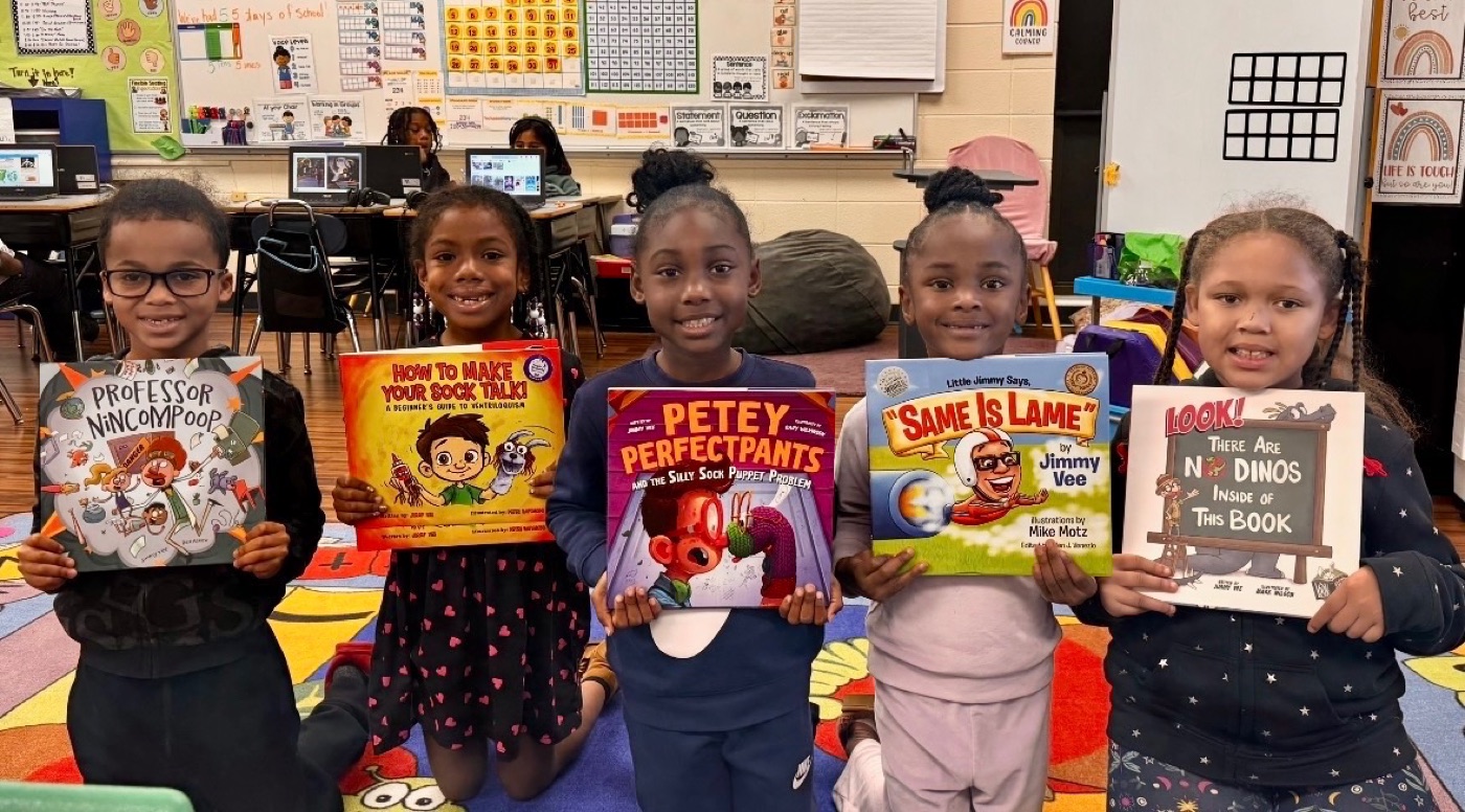 Five elementary students in their classroom, each holding a different Jimmy Vee book